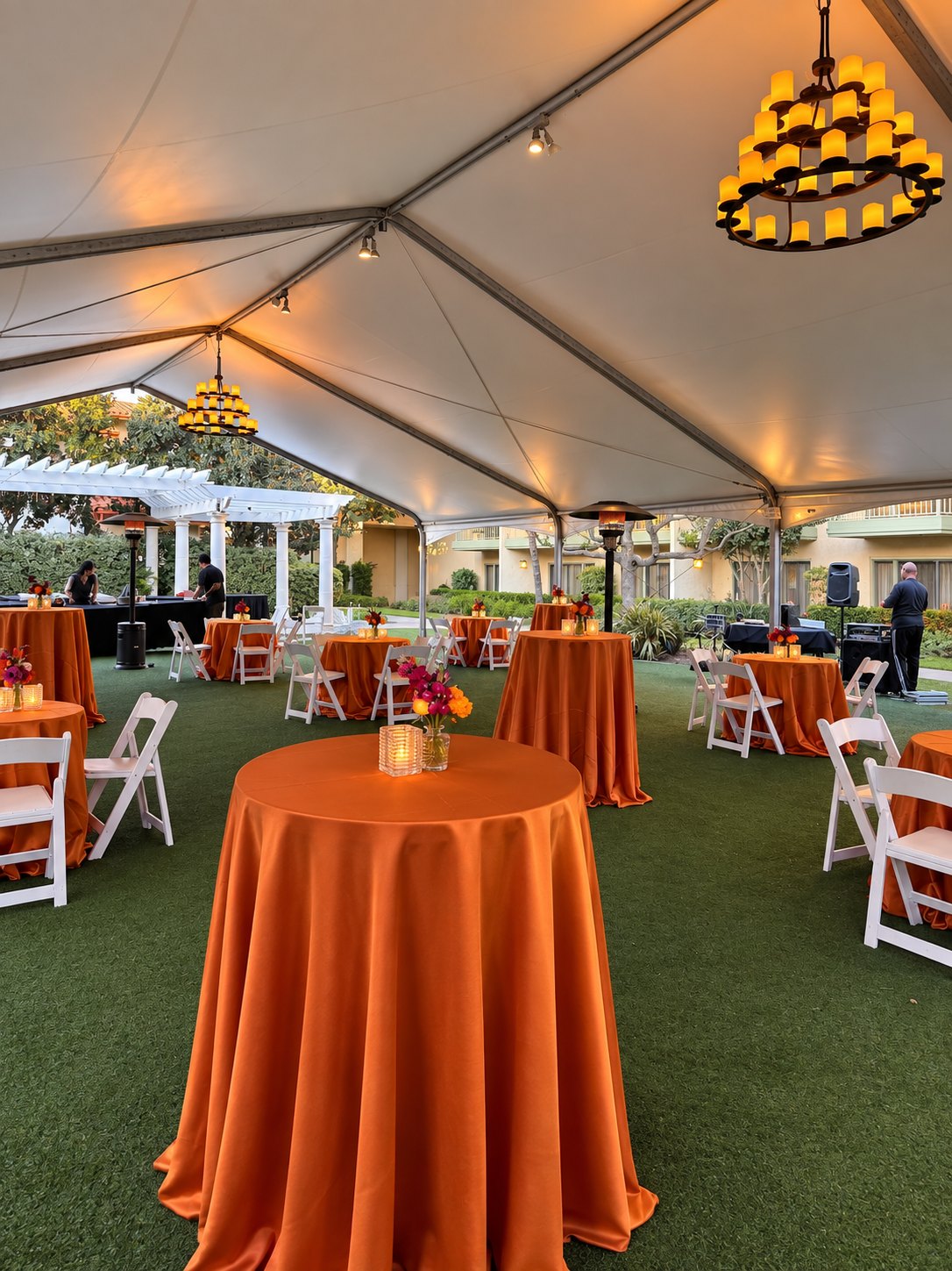 Tented cocktail reception with orange linens and candle chandeliers
